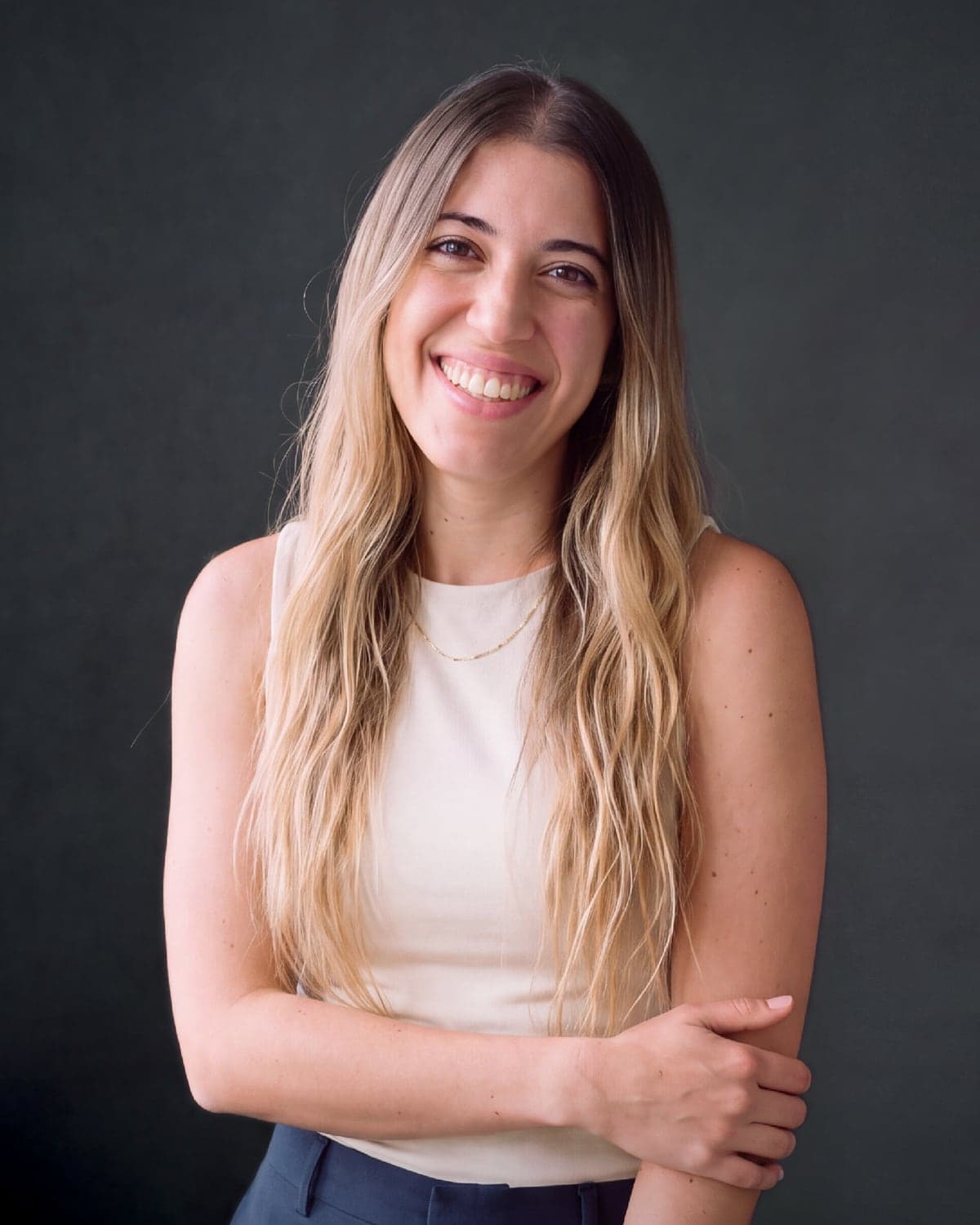 Carla Redón, optometrista y asesora de pacientes de adéu.now, sonriendo con un top claro sobre un fondo oscuro de estudio